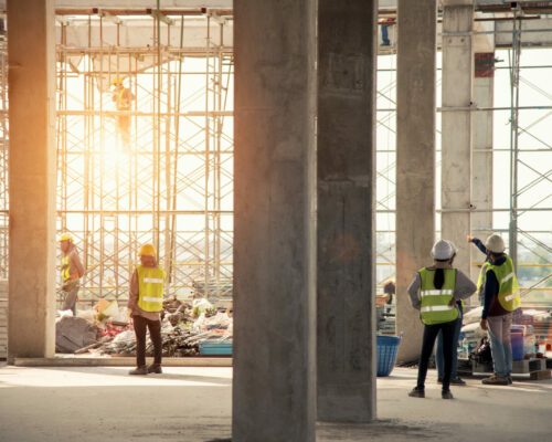 Construction engineers supervising progress of construction project stand on new concrete floor top roof and crane background